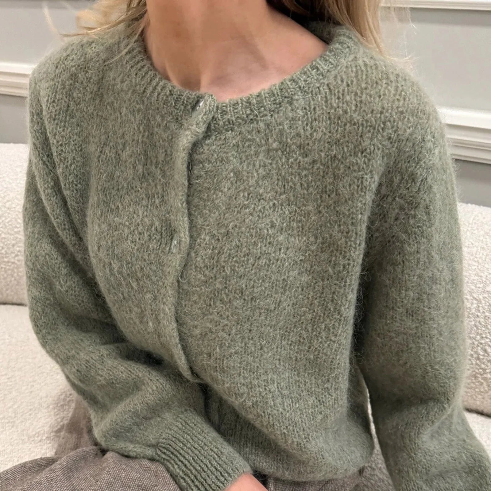 Green knitted sweater worn by a person sitting on a couch.