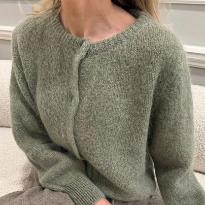 Green knitted sweater worn by a person sitting on a couch.