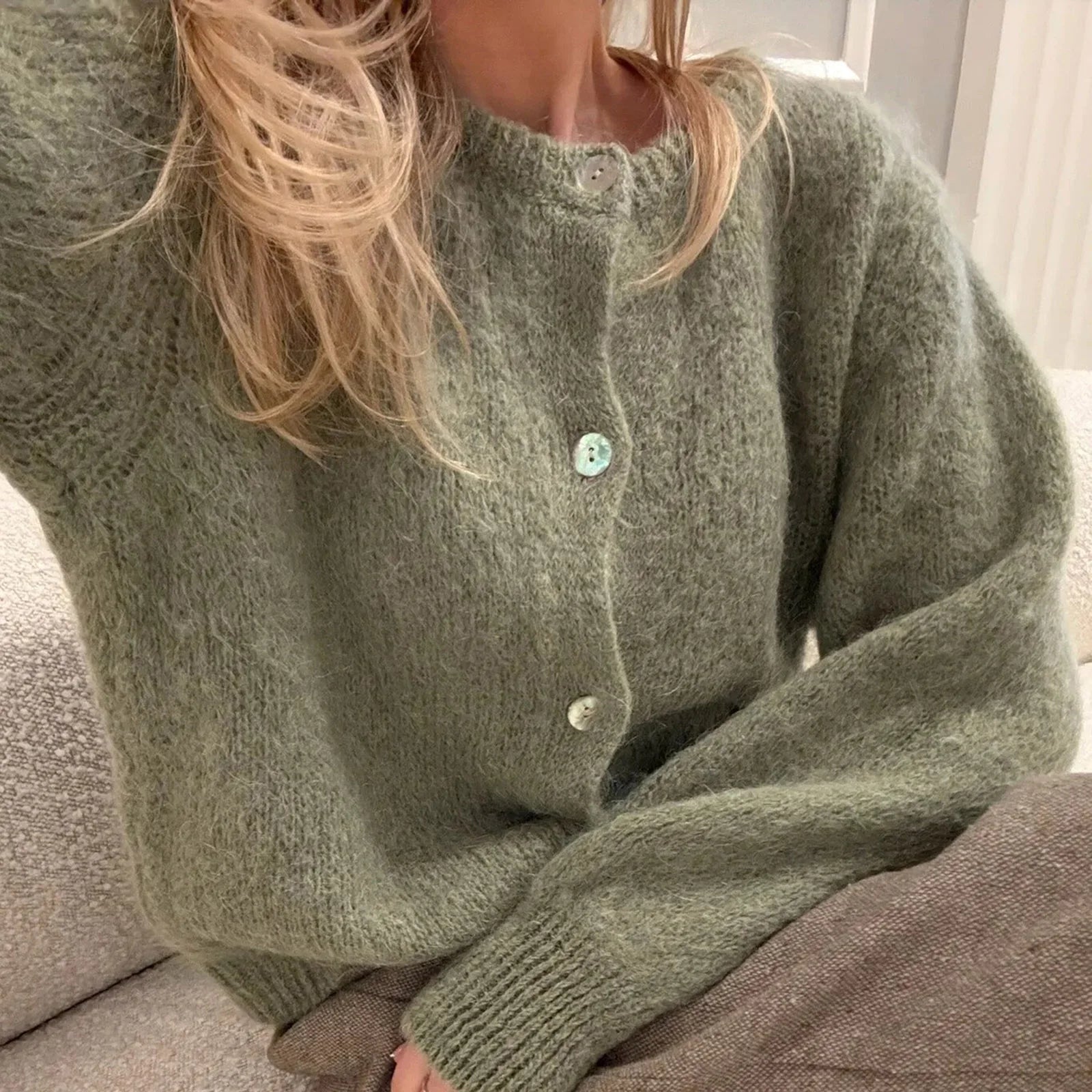 Person wearing a green knitted cardigan sitting on a couch.