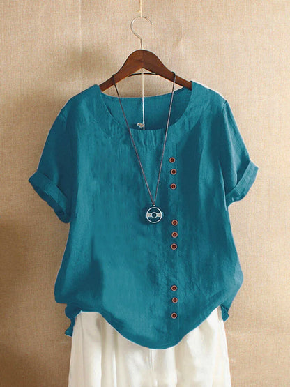 Teal blouse with red buttons on a hanger against a beige background