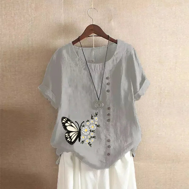 Light gray blouse with butterfly and flower design on a hanger against a beige wall.