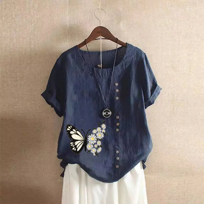 Blue shirt with butterfly and flower design on a hanger against a beige wall