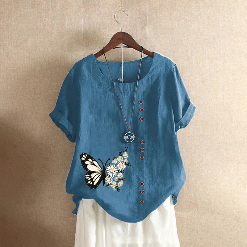 Blue shirt with butterfly and flower design on a hanger against a beige wall