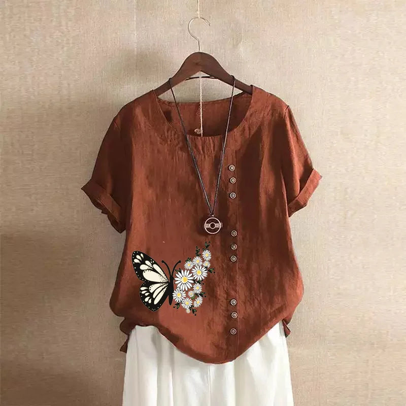 Brown shirt with butterfly and flower design on a hanger against a beige wall.