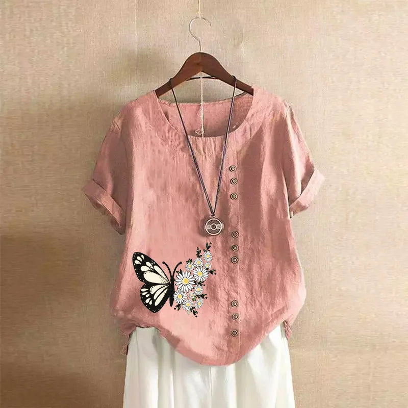 Pink shirt with butterfly and flower design on a hanger against a beige wall.