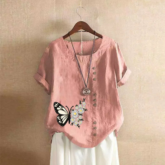 Pink shirt with butterfly and flower design on a hanger against a beige wall.