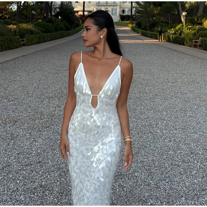 Woman in a silver sequin dress standing on a gravel path with greenery and a building in the background.