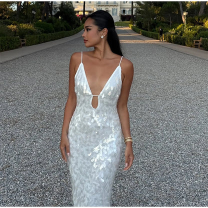 Woman in a silver sequin dress standing on a gravel path with greenery and a building in the background.
