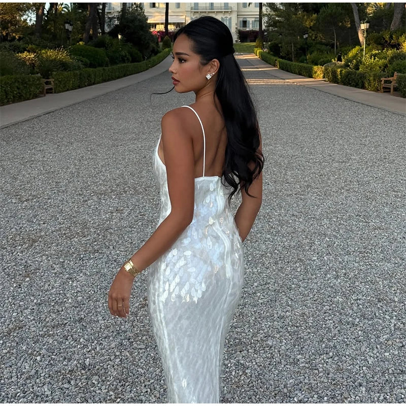 Woman in a white sequin dress walking on a gravel path with greenery in the background