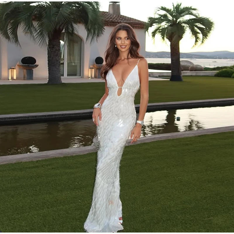 Woman in a white evening gown standing in a luxurious outdoor setting with palm trees and a pool.