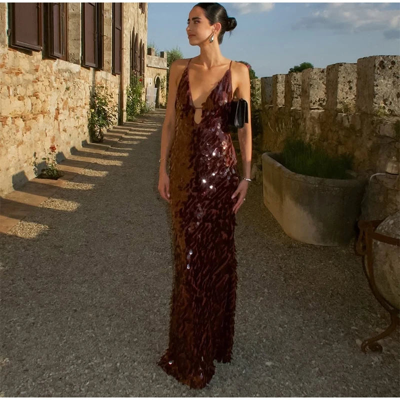 Woman in a dark sequined dress standing in an outdoor setting with stone walls.