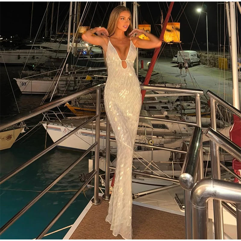 Woman in a white evening gown standing on a dock with boats in the background