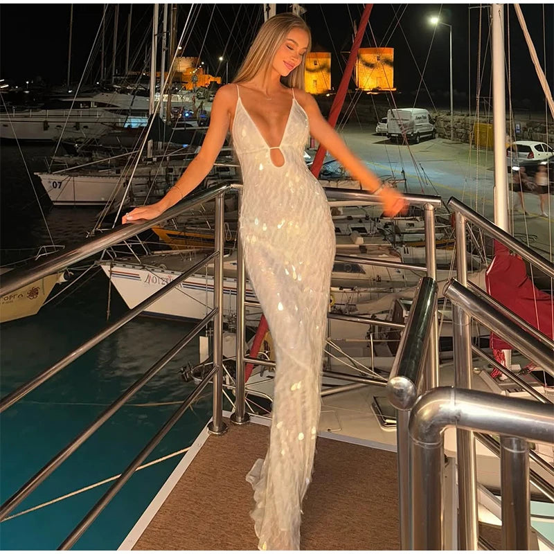 Woman in a white sequin dress standing on a dock with boats in the background