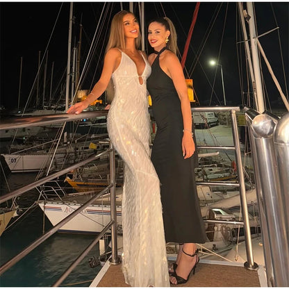 Two women in formal dresses standing on a dock with boats in the background.