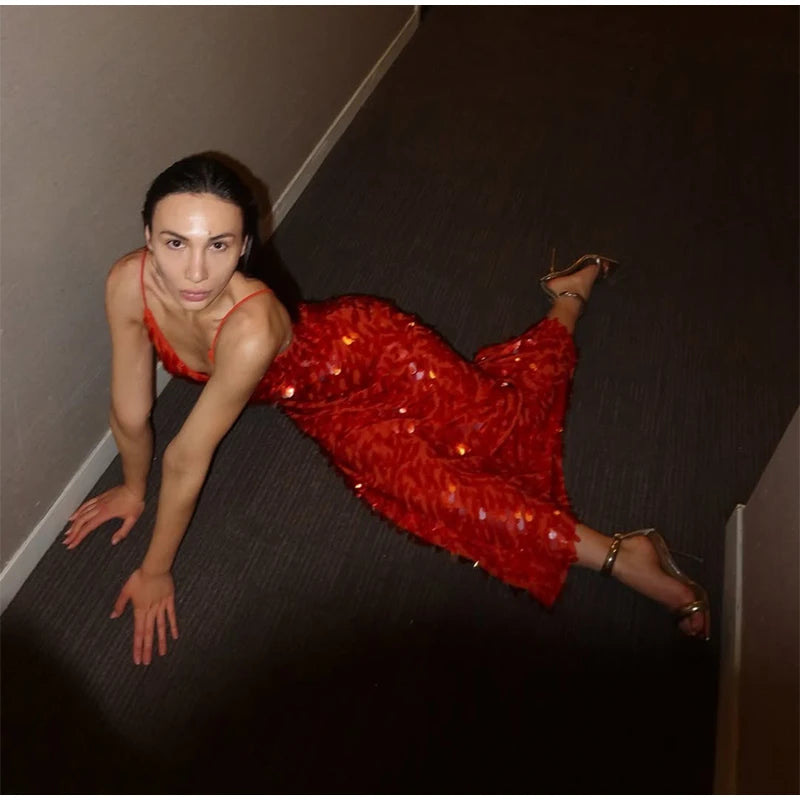 Woman in a red sequin dress posing on a dark floor.