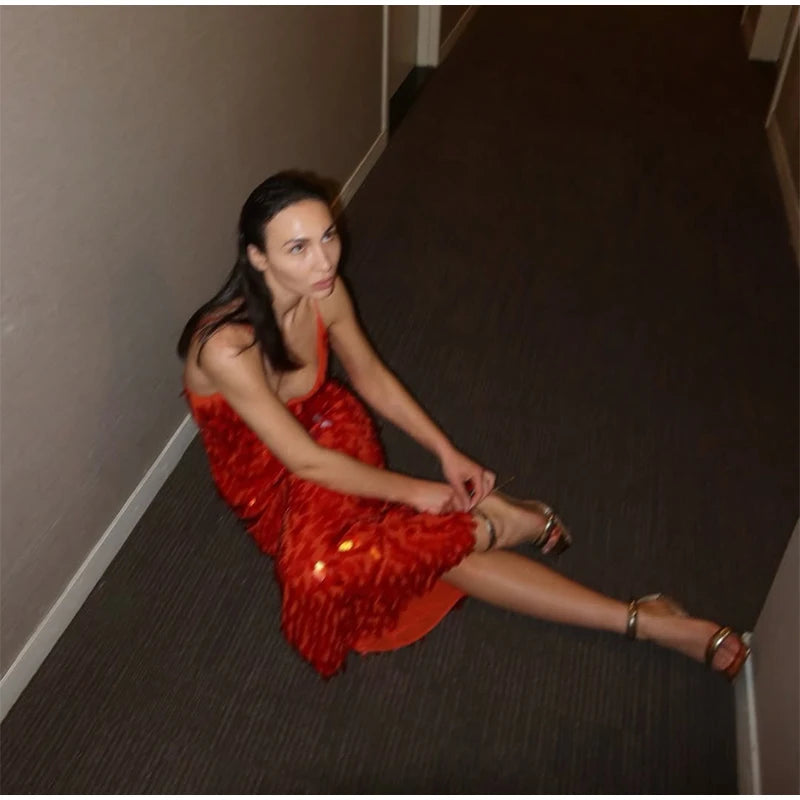 Woman in a red dress sitting on the floor against a plain wall.