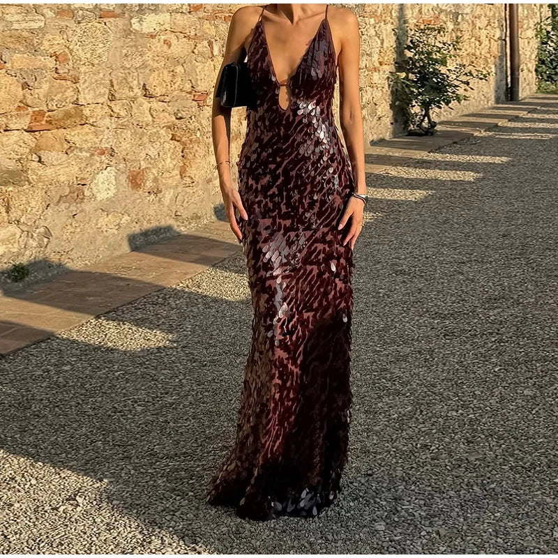 Woman wearing a long, dark sequined dress standing outdoors against a stone wall.