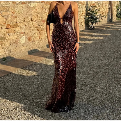 Woman wearing a long, dark sequined dress standing outdoors against a stone wall.