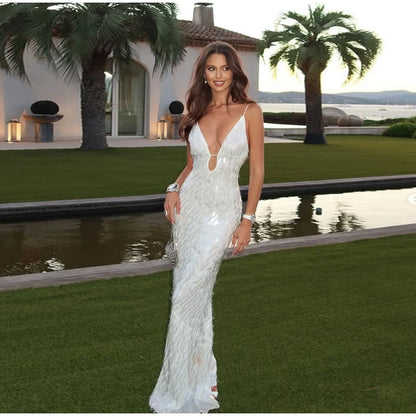 Woman in a white evening gown standing in a luxurious outdoor setting with palm trees and a pool.