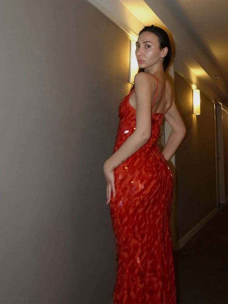 Woman in a red dress standing against a neutral wall.