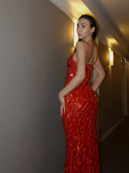 Woman in a red dress standing against a neutral wall.