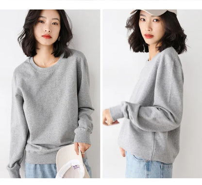 Woman wearing a gray sweater and light blue jeans with a white cap, on a plain background.