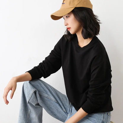 Person wearing a black long-sleeve shirt, light blue jeans, and a beige cap on a plain background