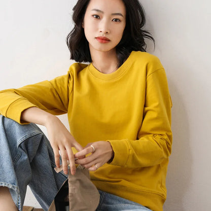 Woman wearing a yellow sweatshirt and blue jeans sitting against a plain background
