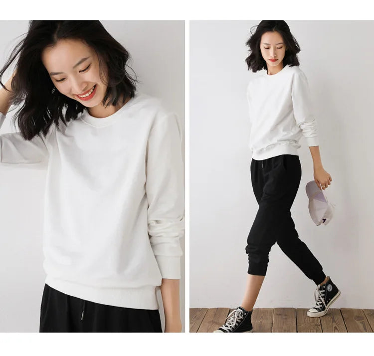 Woman wearing a white sweatshirt and black pants on a plain background