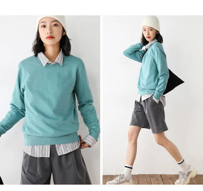 Woman wearing a teal sweater over a striped shirt with gray pants and white sneakers, holding a black bag.