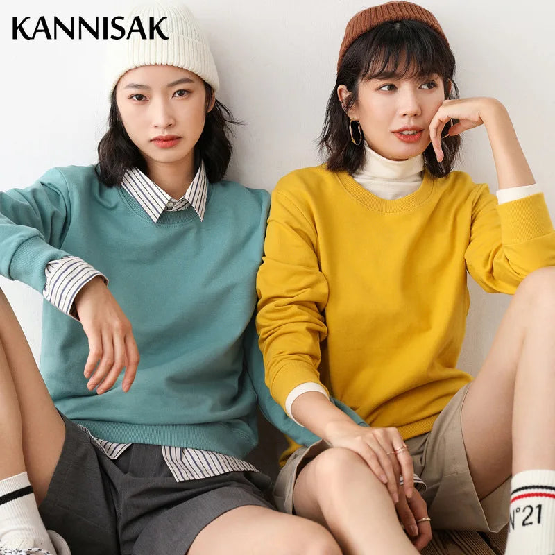 Two women sitting side by side wearing colorful sweaters with 'KANNISAK' branding.