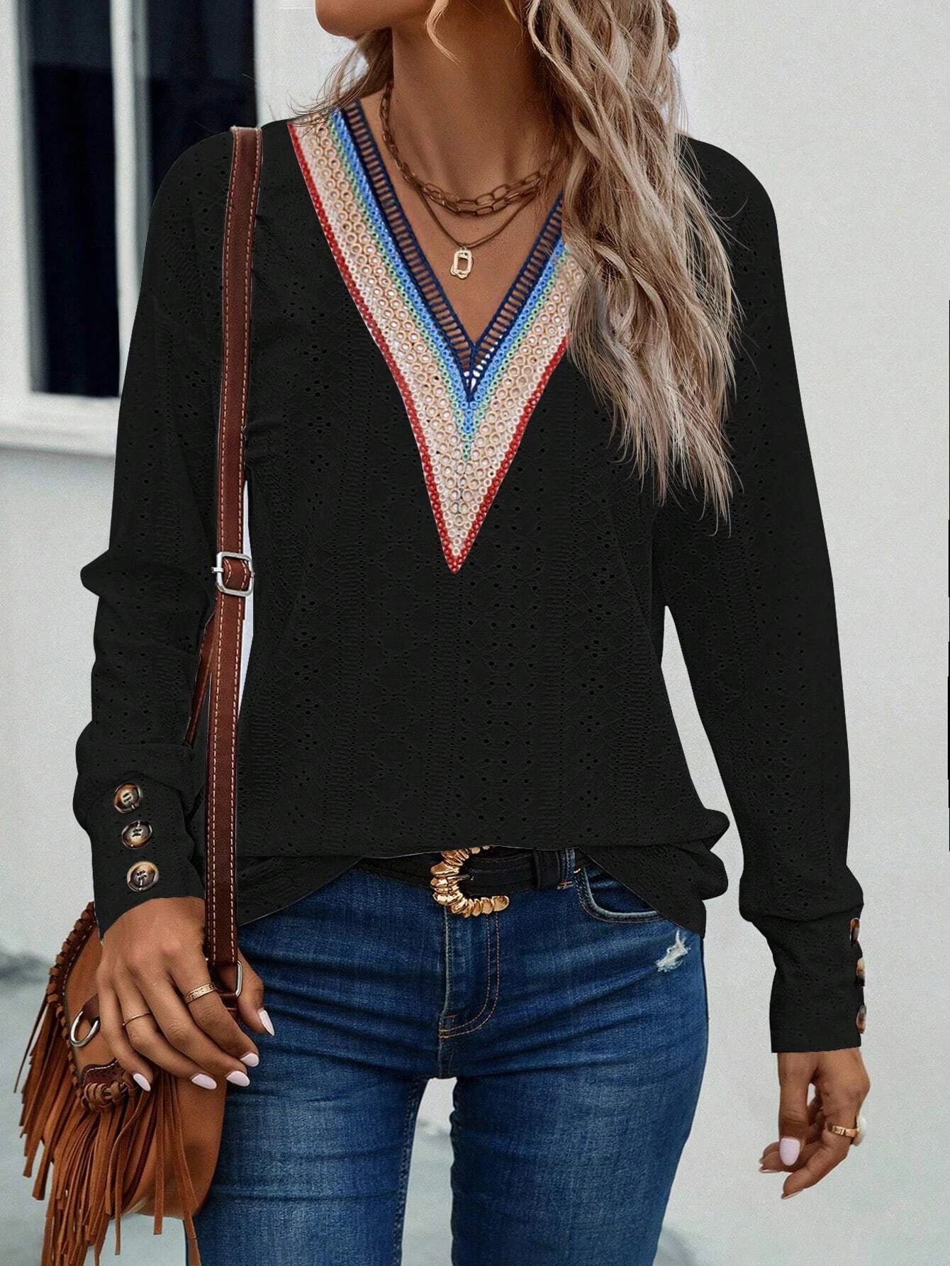 Woman wearing a black long-sleeve top with colorful neckline design, blue jeans, and holding a brown leather bag.