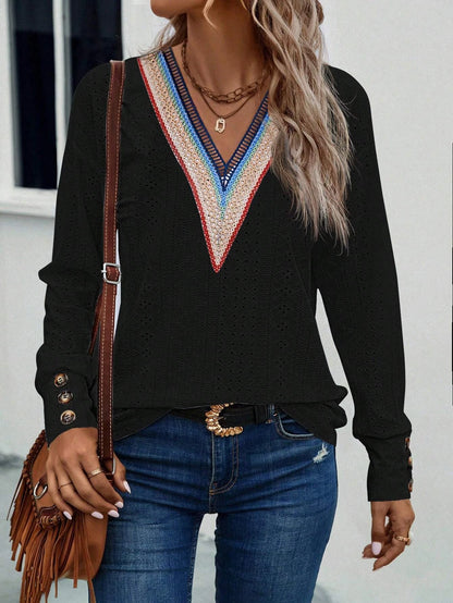 Woman wearing a black long-sleeve top with colorful neckline design, blue jeans, and holding a brown leather bag.