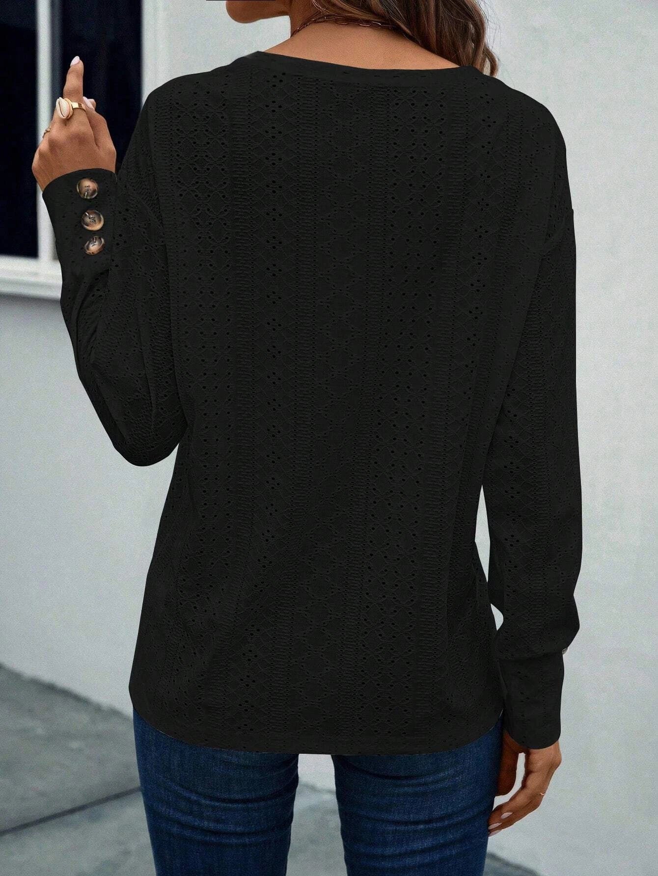 Person wearing a black long-sleeve top with button details on a plain background