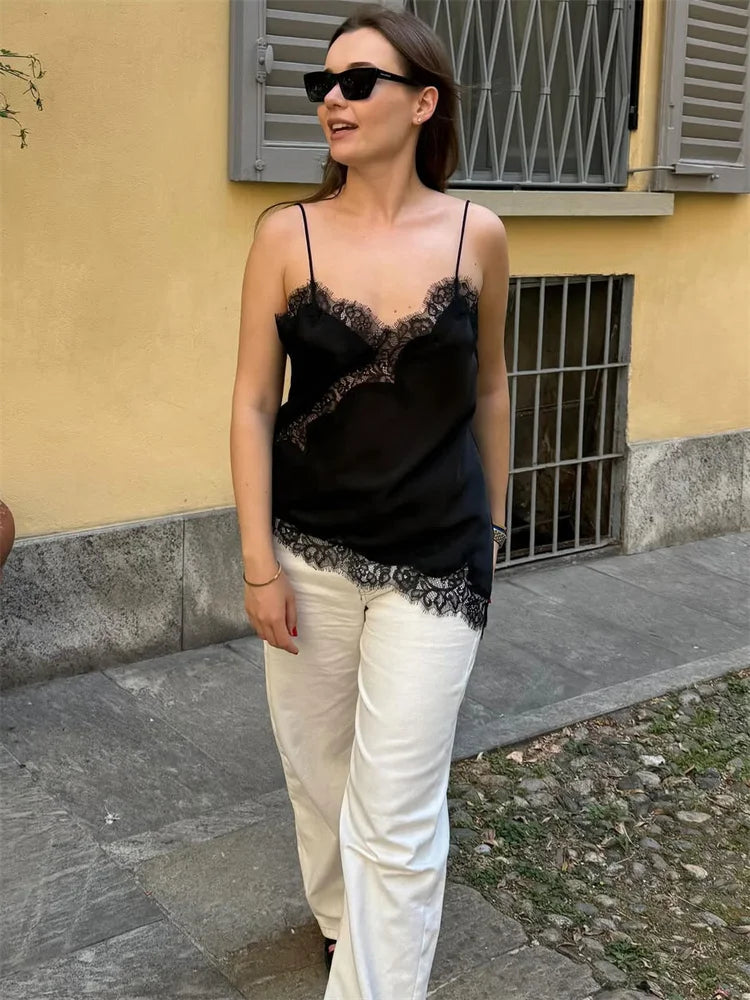Woman wearing a black lace top and white pants standing on a street.