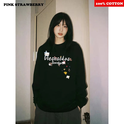 Person wearing a black sweatshirt with graphics and text, standing indoors.