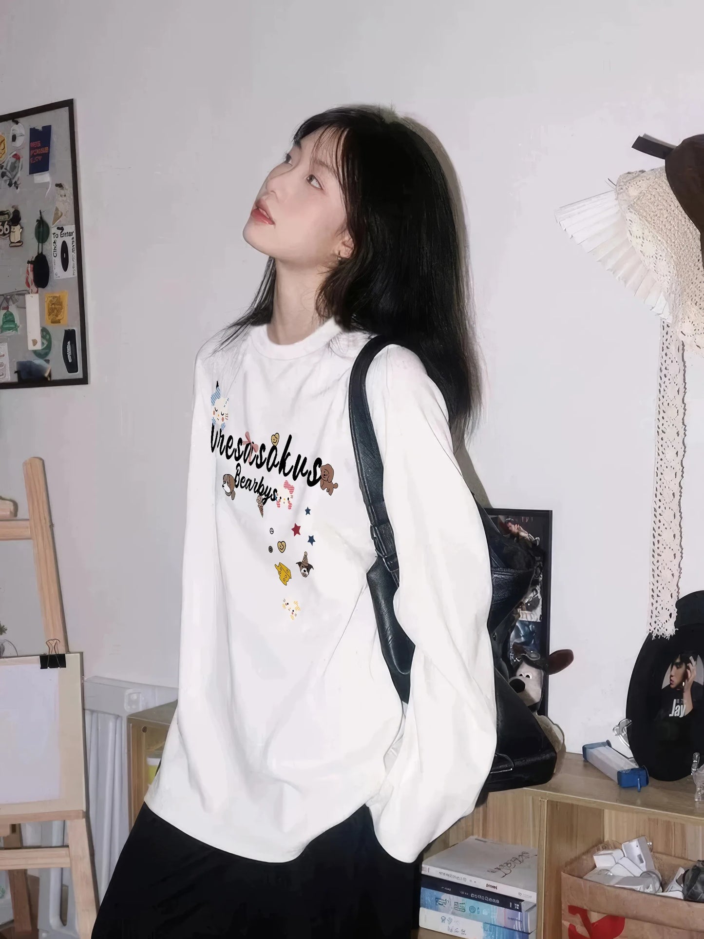 Person wearing a white hoodie with text and graphics, standing in a room with shelves and decor.