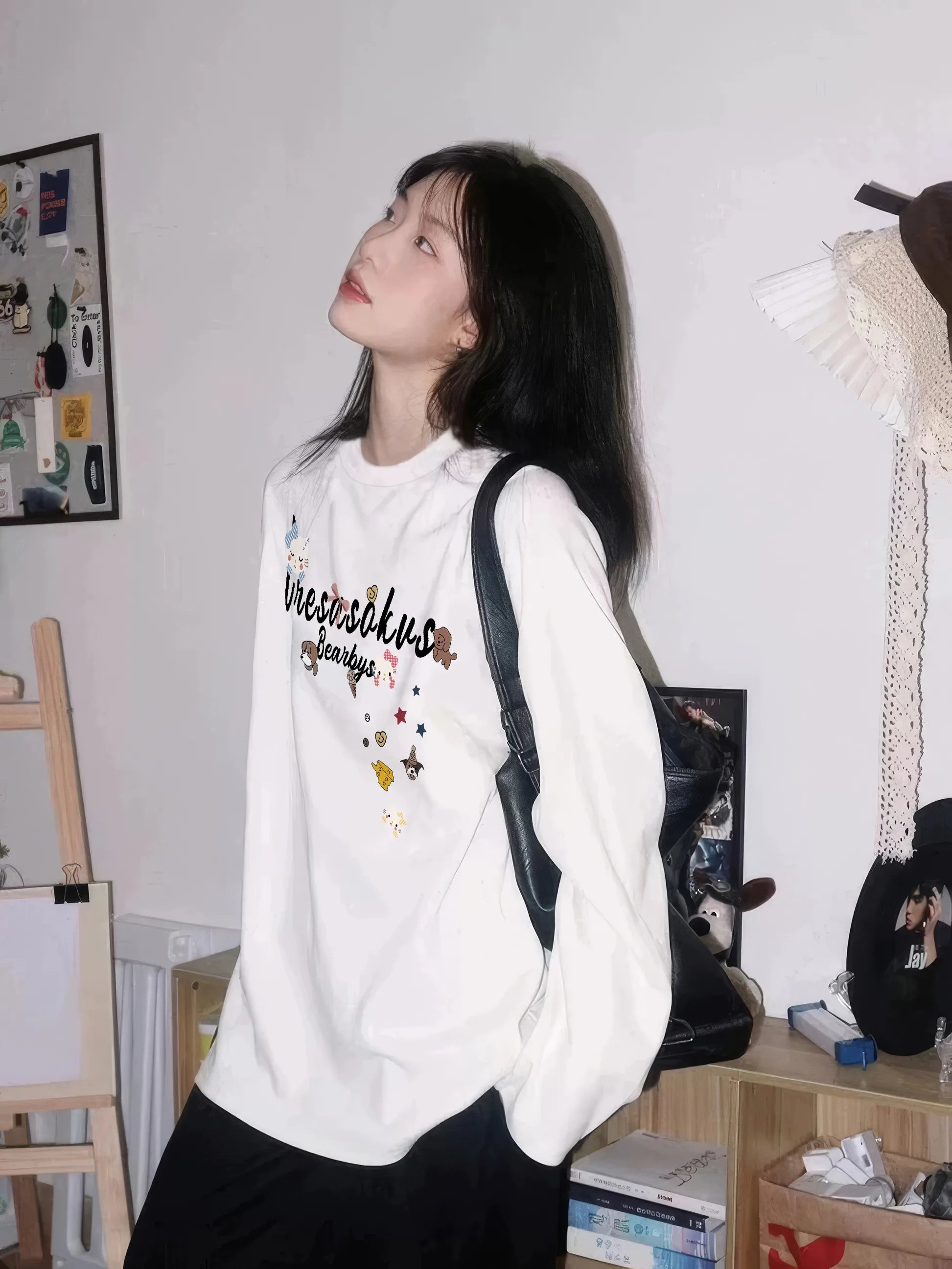 Person wearing a white hoodie with text and graphics, standing in a room with shelves and decor.