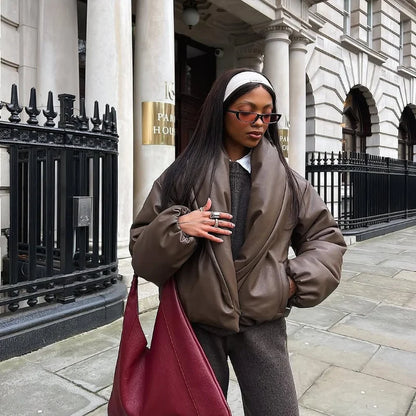 Woman in a brown coat and red bag walking on a city street.
