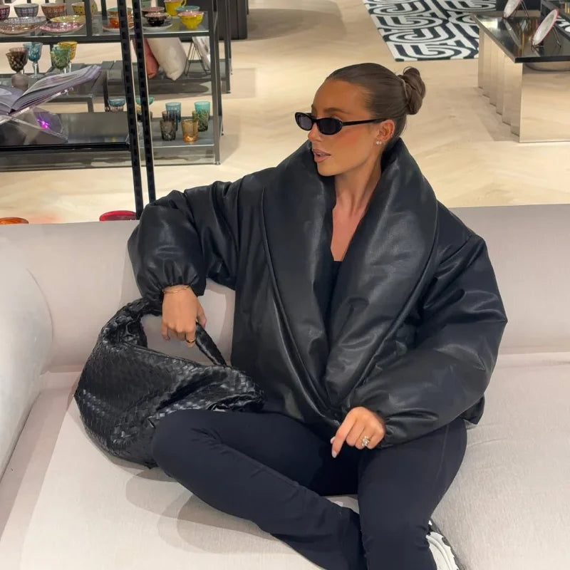Person wearing a black leather jacket and sunglasses, sitting on a couch in a store.