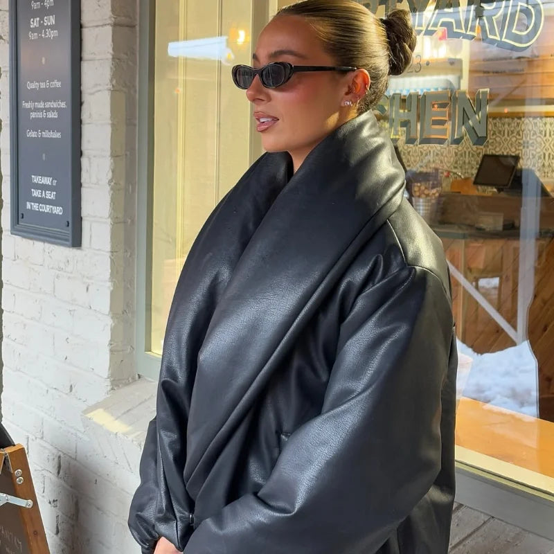 Person wearing a black leather jacket and sunglasses standing in front of a store window.