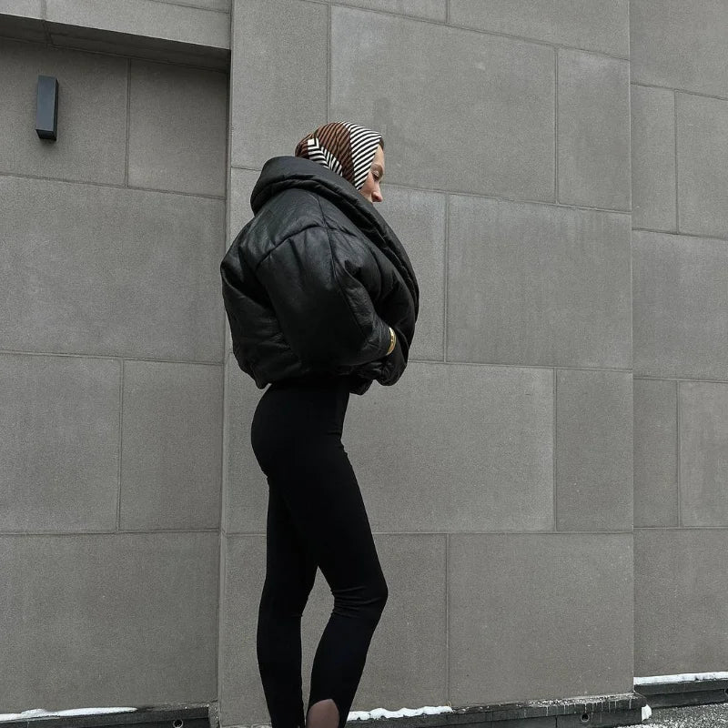 Person wearing a black jacket and leggings against a gray wall