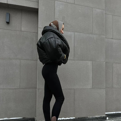 Person wearing a black jacket and leggings against a gray wall
