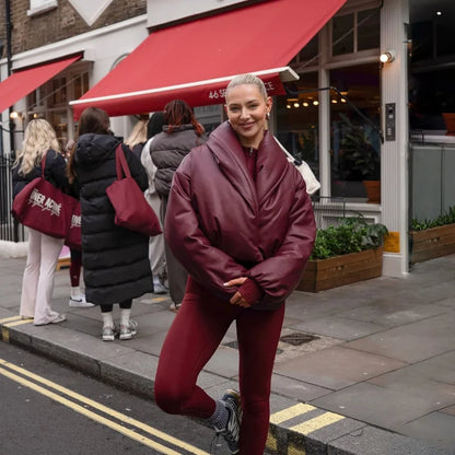 Woman in maroon outfit posing on a street with red awnings and people in the background.