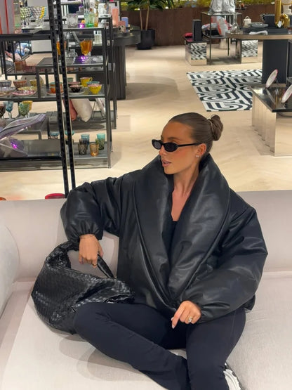 Person wearing a black leather jacket and sunglasses, sitting on a couch in a store setting.