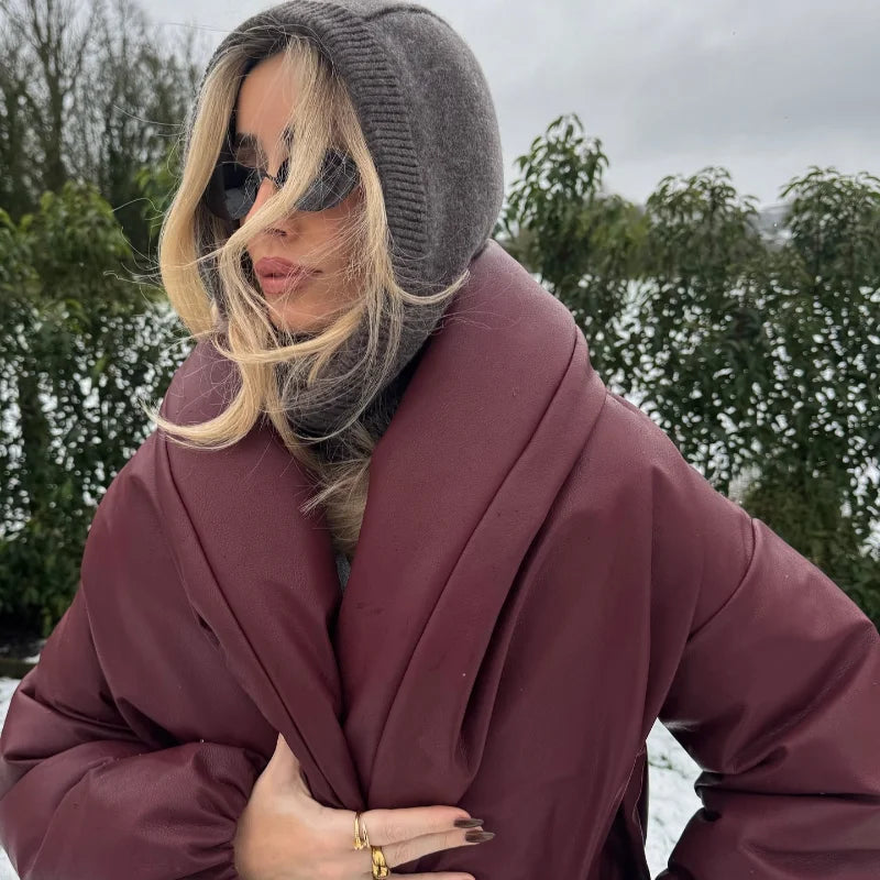 Person wearing a maroon coat and gray knit hat outdoors with trees in the background