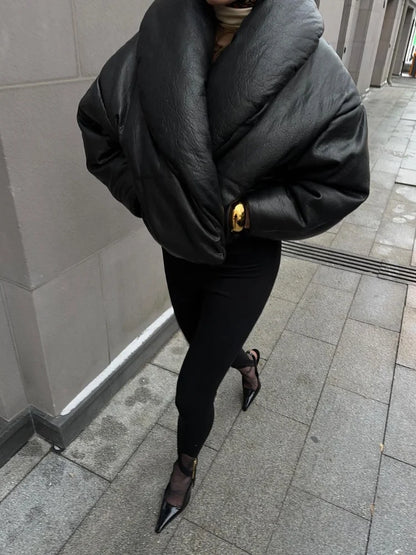 Person wearing a black puffer jacket and black pants on a sidewalk.