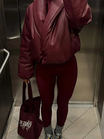Person wearing a maroon jacket and pants holding a matching bag inside an elevator.