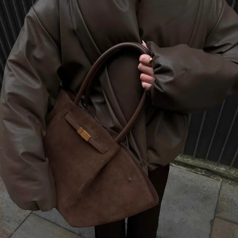 Person holding a brown leather handbag on a city street