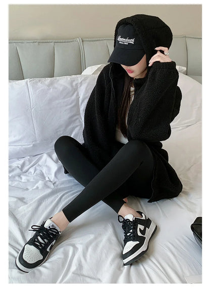 Person wearing a black outfit with a cap sitting on a bed.